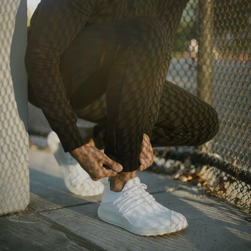 a man tying his white tennis shoes on the sidewalk