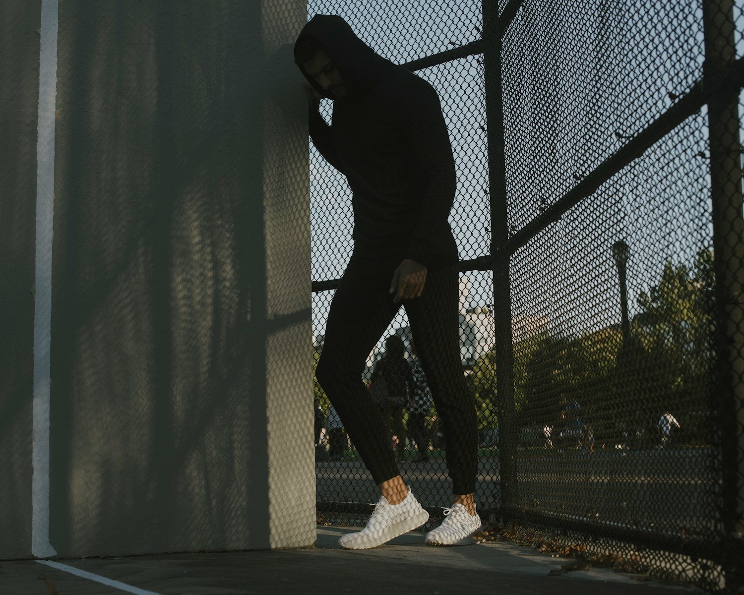 a man in a black hoodie leaning against a fence